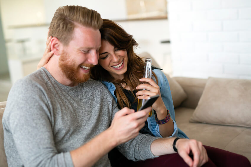 Gut aussehendes Paar chillt im Wohnzimmer und nutzt gemeinsam ein Smartphone
