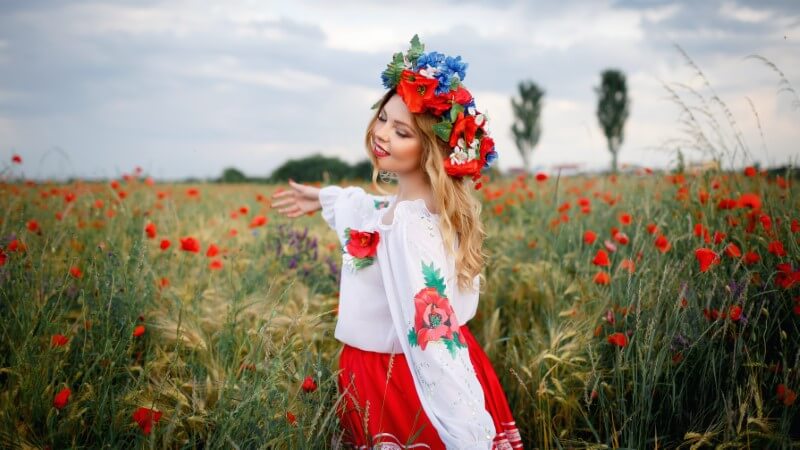 Schöne ukrainische Frau in traditioneller Kleidung mit Blumenkrohne in einem Mohnfeld